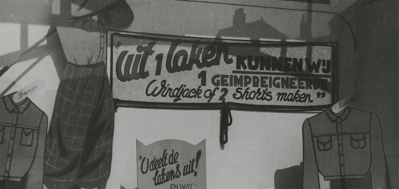 1944, Spui 258-264, Firma Van der Stigchel: 'Uit 1 laken kunnen wij 1 geïmpregneerde windjack of 2 shorts maken' | fotograaf: M. Huizinga
